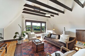 A cozy loft-style living room with a large window, wooden beams, a patterned rug, and a comfortable seating area. - The Pearl, NH hidden luxury close to the Quinnipiac River in historic property (New Haven)