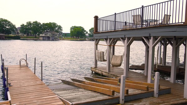 A wooden dock leading to a pier with a hammock and chairs on the upper level.