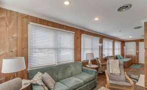 A cozy living room with a green sofa, a wooden accent wall, and a lamp. - Quaint Beach Block Cottage, 100 steps to the beach (Dewey Beach)
