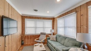 Una habitación acogedora con paredes de paneles de madera, un sofá verde, una mesa de centro de madera, una silla y un televisor montado en la pared.