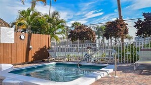 A swimming pool with a wooden fence and metal railings, surrounded by palm trees and a clear sky. - MarcoView 402 - A Slice of Paradise! Premier Waterfront Location @Anglers Cove! (Marco Island)
