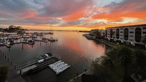 A marina with boats docked, a dock with a boat ramp, and a building with arched windows. - MarcoView 402 - A Slice of Paradise! Premier Waterfront Location @Anglers Cove! (Marco Island)