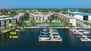 A marina with boats docked, a large building with multiple floors, and a clear view of the ocean. - MarcoView 402 - A Slice of Paradise! Premier Waterfront Location @Anglers Cove! (Marco Island)