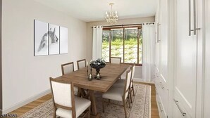 Een eetkamer met een houten tafel, witte stoelen, een kroonluchter en een groot raam met gordijnen.