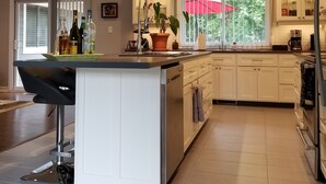 A modern kitchen with a central island, pendant lighting, and a view of the outdoors through large windows. - Alba Cottage with Brand New Pool  (Niagara-on-the-Lake)