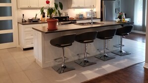 A modern kitchen with white cabinets, a central island with bar stools, stainless steel appliances, and pendant lighting. - Alba Cottage with Brand New Pool  (Niagara-on-the-Lake)