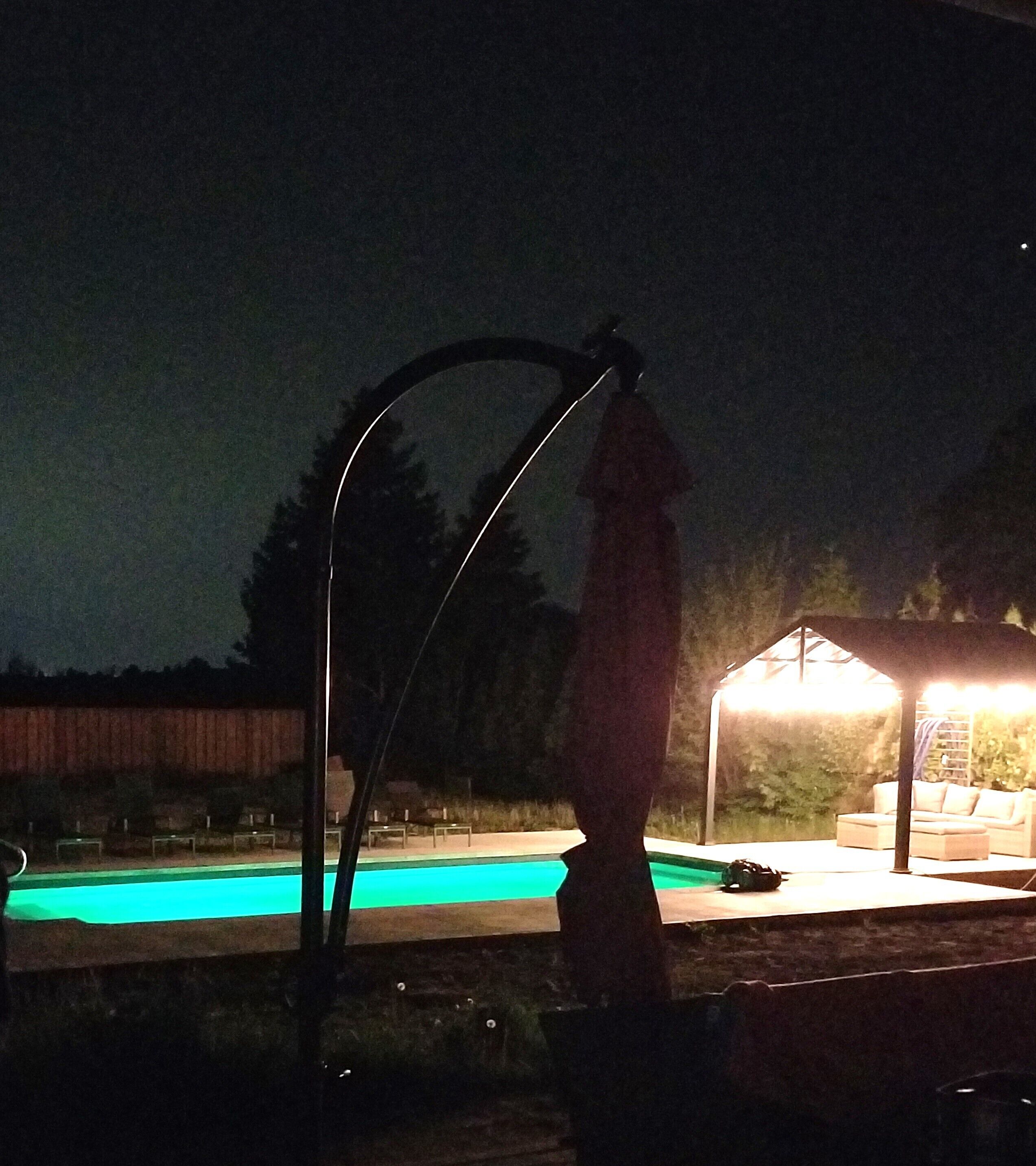 A nighttime view of a swimming pool area with a gazebo and a statue.