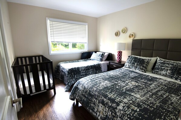 Een slaapkamer met twee bedden, een ledikant, een raam met zonwering, een nachtkastje met een lamp en decoraties aan de muur.