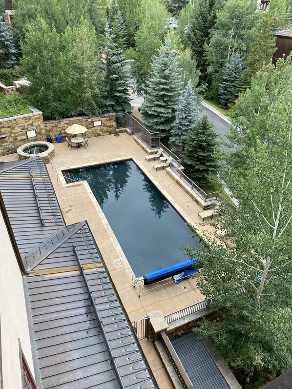 Ein rechteckiger Pool mit einer Steindeck, umgeben von einem Metallzaun und einer Steinmauer mit Feuerstelle.