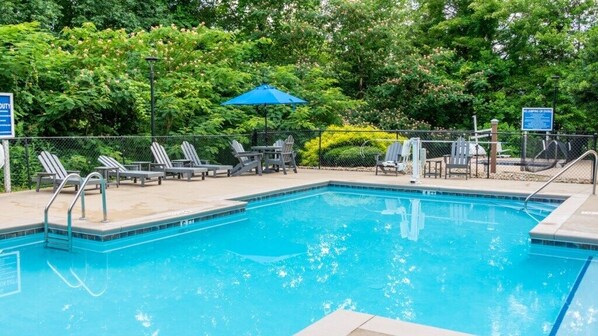 Relax by the pool surrounded by lush greenery and shaded by an umbrella.