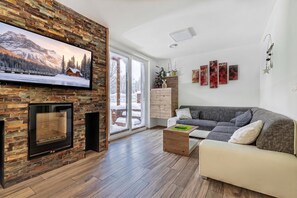 A modern living room with a stone fireplace, a large flat-screen TV, a sofa, and a coffee table. - Pool Villa Katja near Kranjska Gora, Gozd Martuljek, Slovenia (Gozd Martuljek)