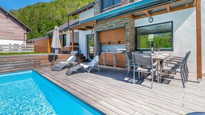 Une maison moderne dotée d’une piscine, d’un espace salon extérieur et d’une cheminée en pierre.