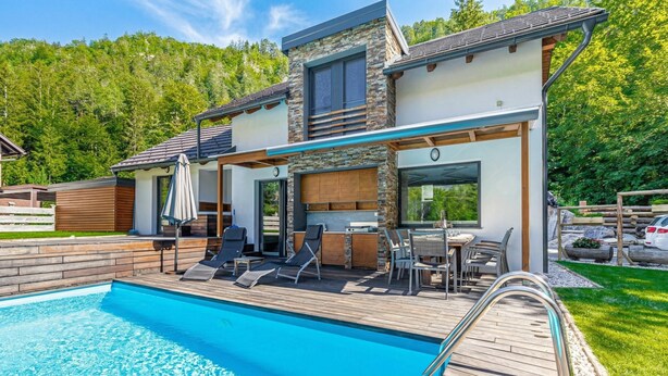 Une maison moderne dotée d’une piscine, d’un espace salon extérieur et offrant une vue sur une zone boisée.