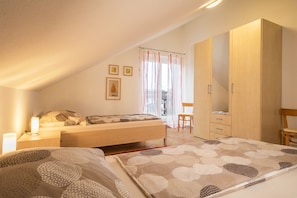 Une chambre à coucher comprenant un lit, une table de chevet, une lampe, une armoire et donnant sur l’extérieur.