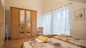 Ein Schlafzimmer mit einem Bett, einem Holzschrank, einem Stuhl und einem Fenster mit Vorhängen.