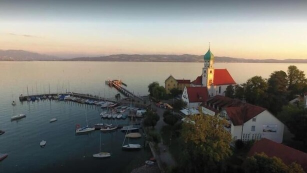 Ein Anwesen am Wasser mit Anlegesteg, Booten und einer Kirche mit Turm.