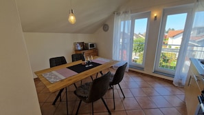 Un coin repas comprenant une table en bois, des chaises, une horloge, un four à micro-ondes et une vue sur l’extérieur.