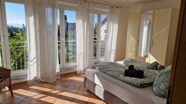 A bedroom with a large bed, a wardrobe, and a balcony with curtains.