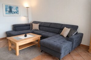 Um sofá seccional cinza com uma mesa de centro de madeira, uma almofada estampada e um quadro na parede.