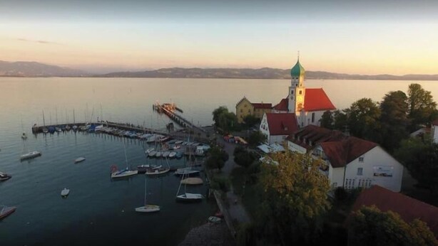 A waterfront property with a dock, boats, and a church with a tower. - Apartment 'Haus Sonnenseite Säntis' with Mountain View, Balcony and Wi-Fi (Wasserburg)