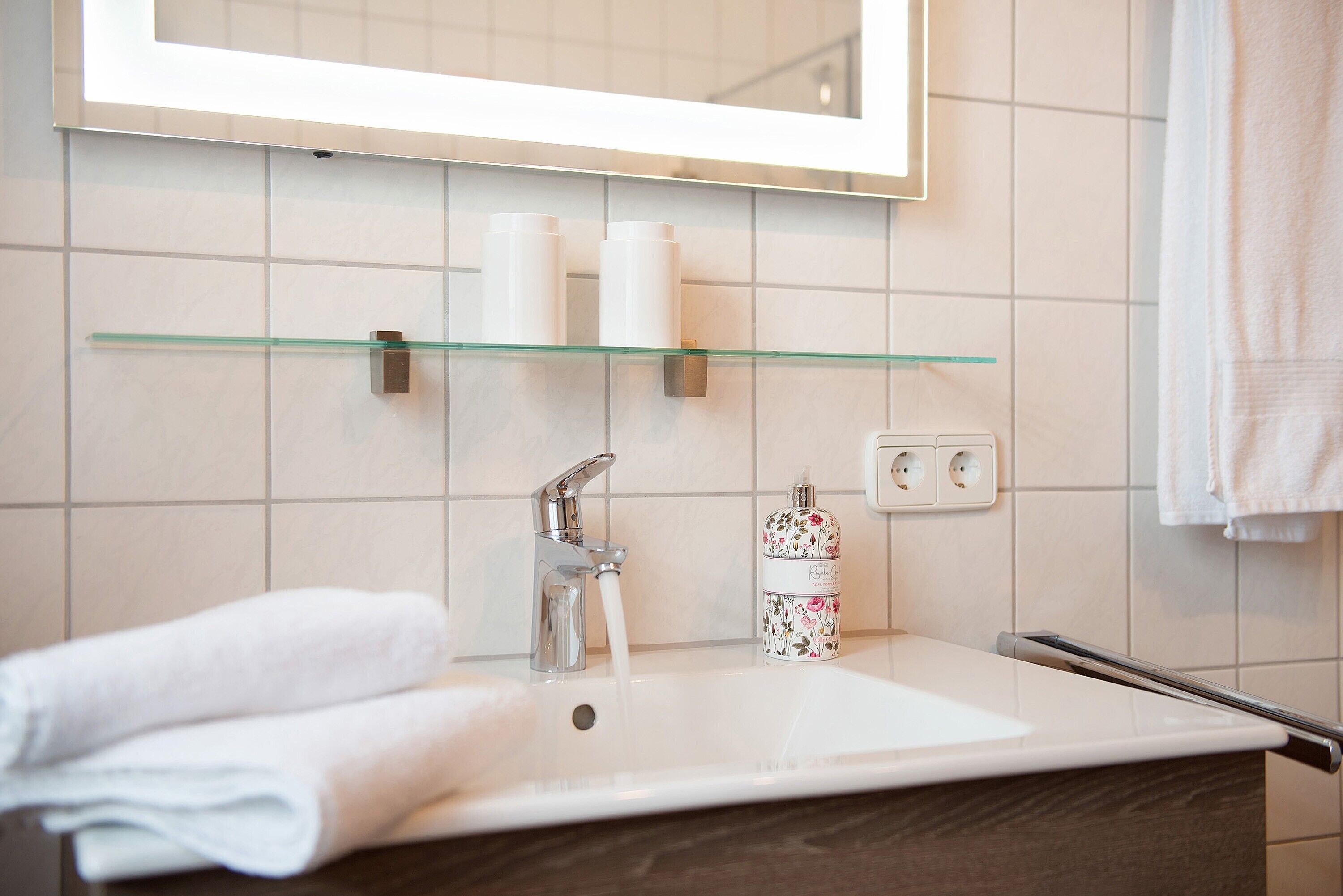 A bathroom with a white sink, a glass shelf above it, a mirror, and a towel on the counter.