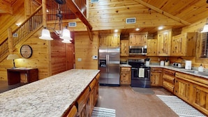 A wooden cabin interior with a kitchen featuring a granite countertop, stainless steel appliances, and wooden cabinets.