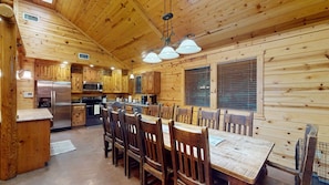 A wooden cabin interior with a dining area, kitchen, and a large window. - Winding Creek Lodge 5+ Bedroom 5 Bathroom w/ Gameroom Near Broken Bow Lake! (Broken Bow)