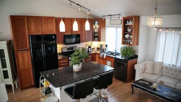Eine moderne Küche mit Holzschränken, einem schwarzen Kühlschrank, einer Mikrowelle und einem Essbereich mit Barhocker und Couchtisch.