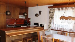 A compact kitchen with wooden cabinets, a central island, and a dining area with striped chairs. - Tgèsa Palits Seehuber by Interhome (Sedrun)
