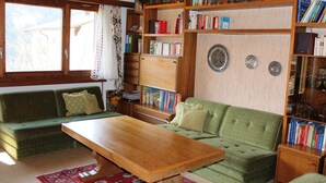 A cozy living room with a green sofa, a wooden coffee table, and a bookshelf filled with books. - Tgèsa Palits Seehuber by Interhome (Sedrun)