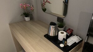 Habitación de hotel con un mostrador de madera, cafetera, rollo de papel higiénico, planta pequeña y espejo.