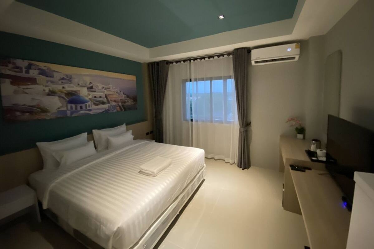 Ein Hotelzimmer mit einem großen Bett, einem Fernseher, einem Schreibtisch und einem Bild an der Wand.