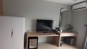 Habitación compacta con escritorio, televisión, refrigerador pequeño y aire acondicionado.