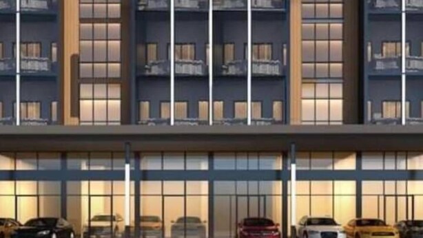 Un hotel moderno con varios pisos, amplias ventanas y una fila de coches aparcados en la entrada.