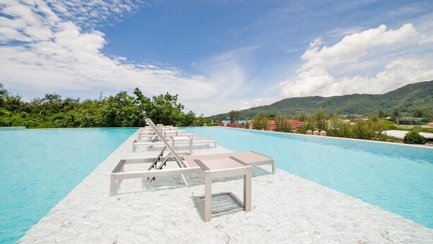 Zona junto a la piscina con sillones de descanso y vistas a un paisaje montañoso.