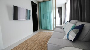 Una sala de estar moderna con un sofá gris, un televisor de pantalla plana montado en la pared y un puerta corrediza de vidrio que da a un balcón.