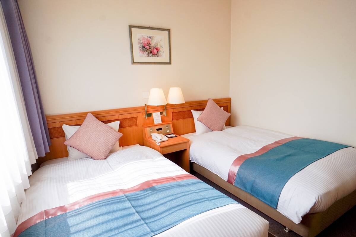 A hotel room with two beds, a wooden headboard, a nightstand with a lamp, and a framed picture on the wall.