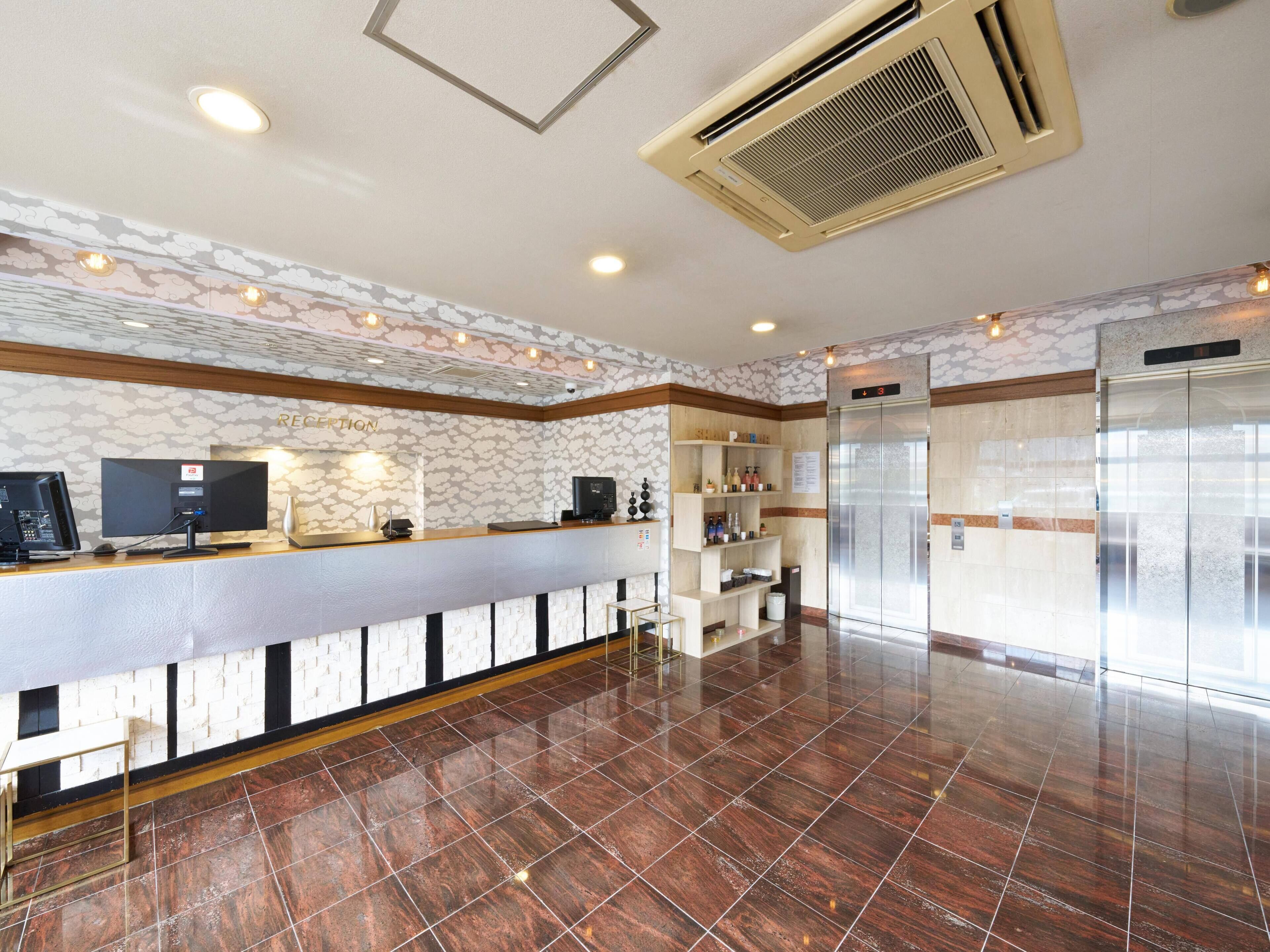 A reception area with a reception desk, a digital screen, a coffee machine, and a wall-mounted air conditioner.