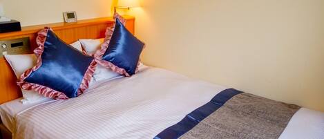 Una camera d'albergo con un letto, cuscini, un comodino, una lampada e una sveglia.