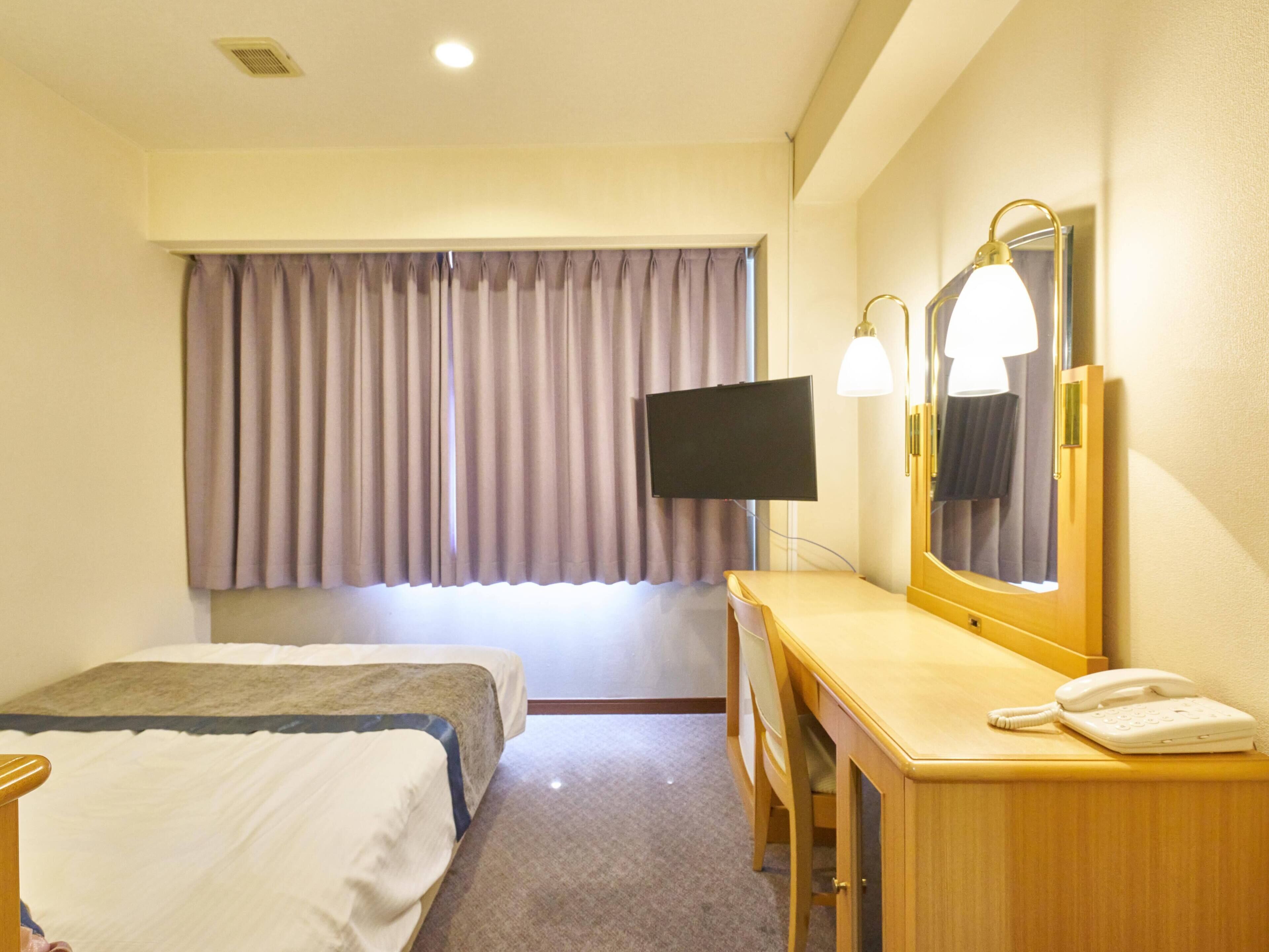 A hotel room with a bed, a desk with a telephone, a mirror, and a television on the wall.