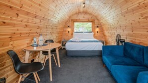 A cozy, wooden-paneled room with a bed, a blue sofa, a small table with chairs, and a window providing natural light. - Coromandel Shelly Beach TOP 10 Holiday Park (Coromandel)
