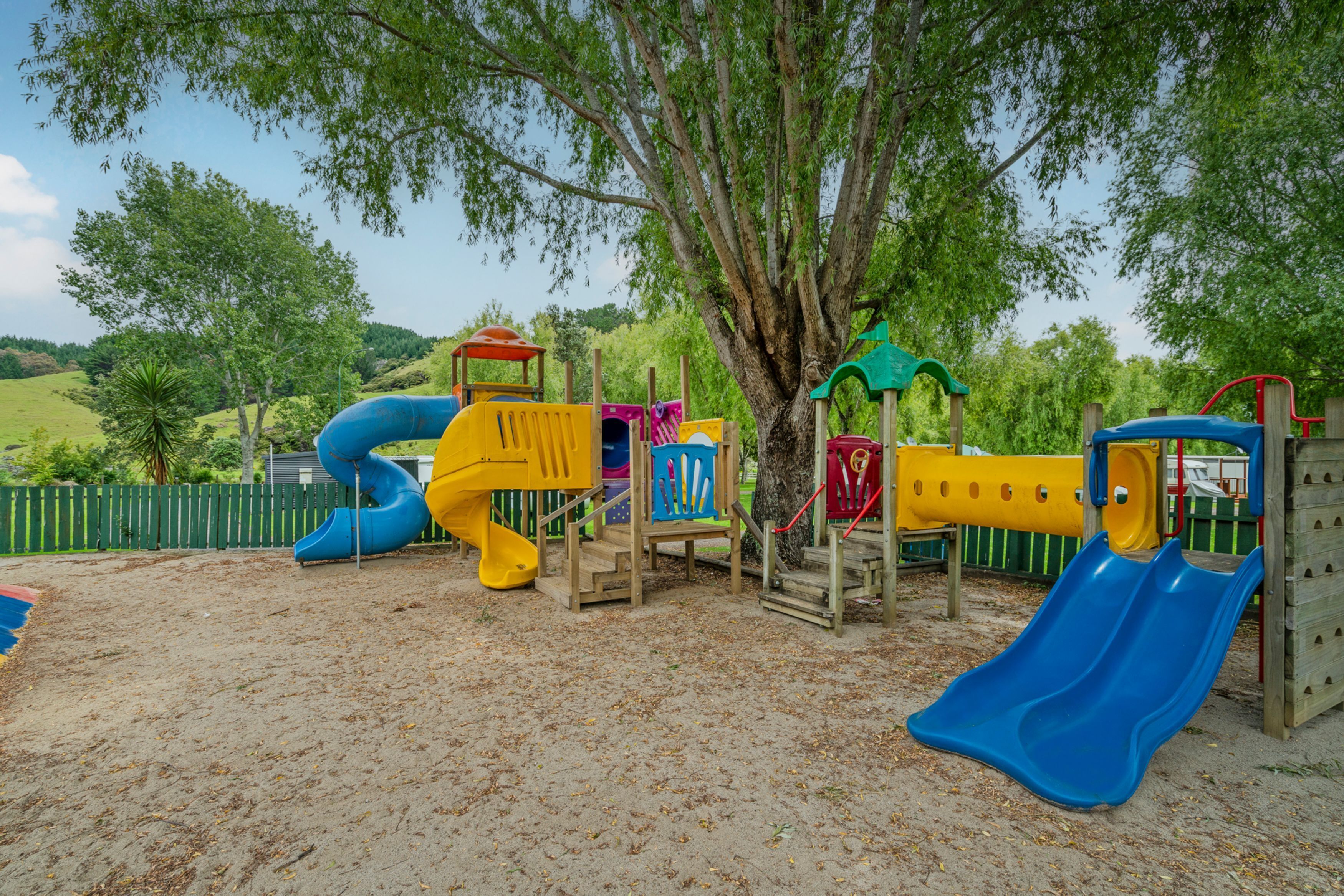 Un parque infantil con toboganes y estructuras para escalar, rodeado de árboles.