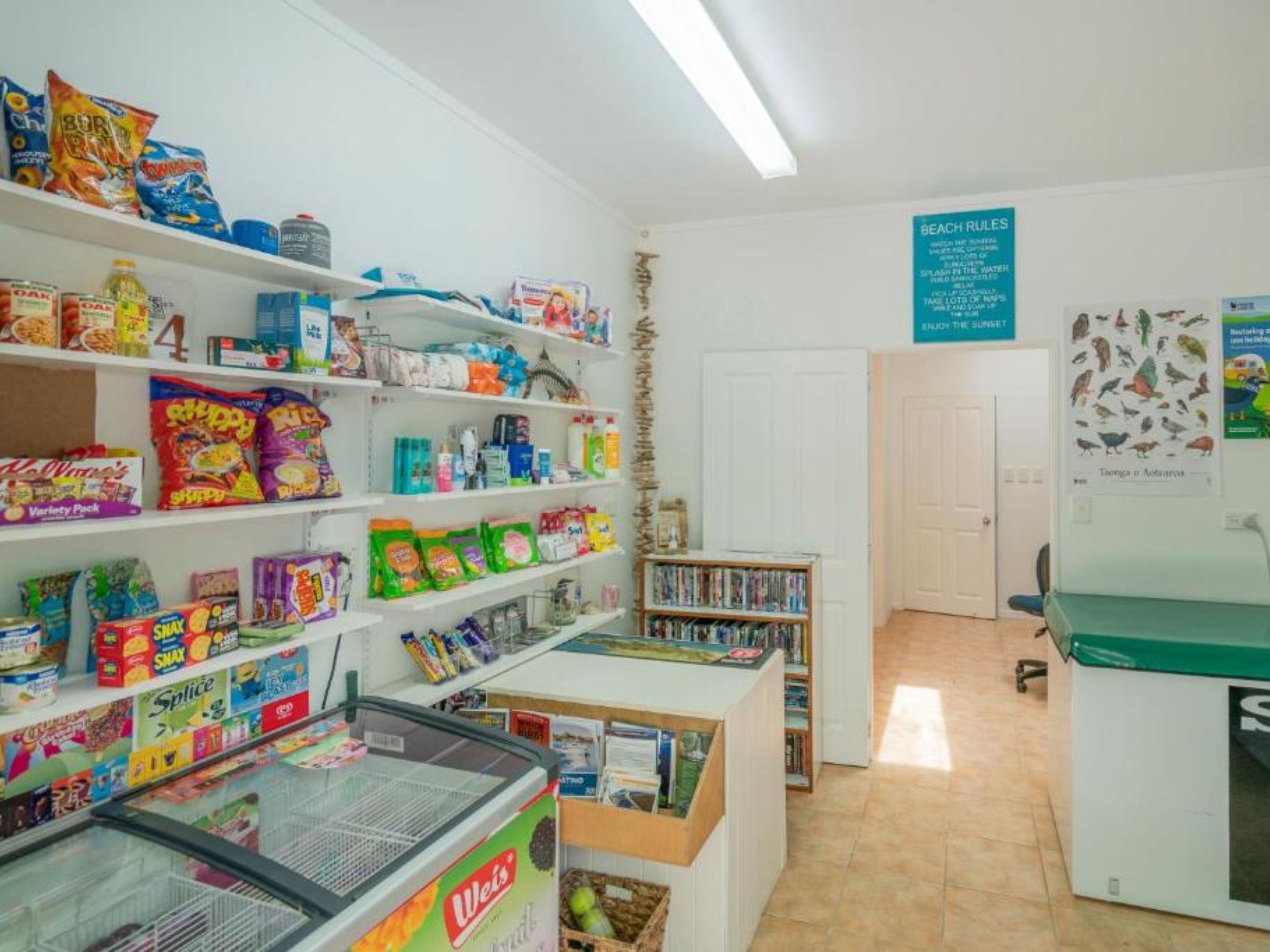 Una tienda de comestibles con estantes llenos de refrigerios, bebidas y artículos del hogar.