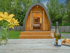 Ein gemütliches, halbrundes Holzhaus mit Bett und kleinem Tisch, umgeben von viel Grün.