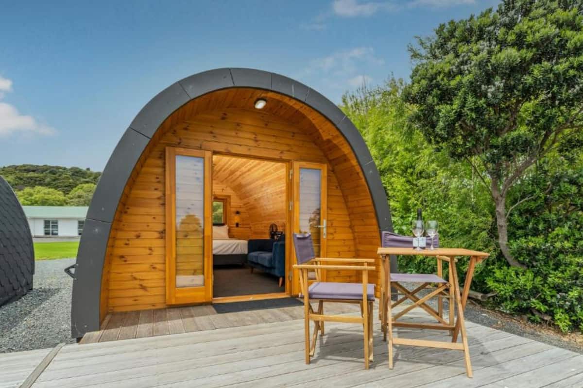 Una cabaña de madera acogedora y parcialmente abierta, con una cama, una mesita y sillas en una terraza de madera.