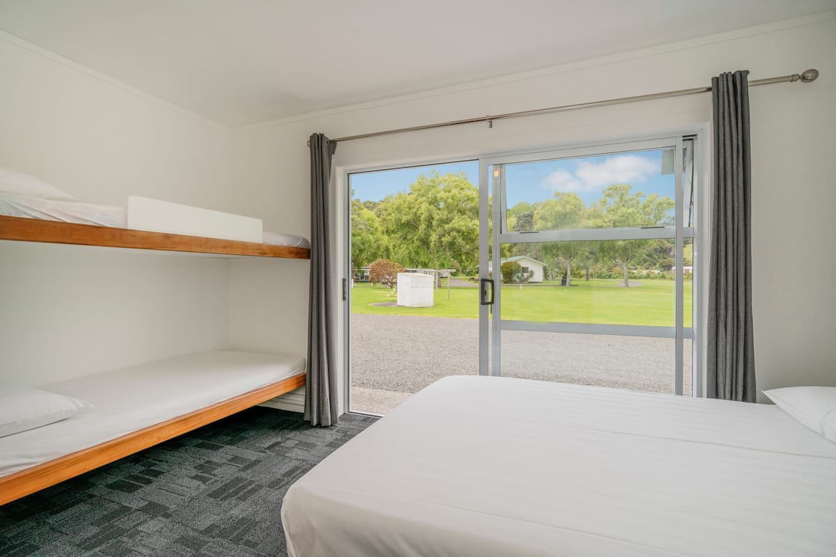Habitación de hotel con literas, una cama individual y un amplio ventanal corredero que da a un jardín.