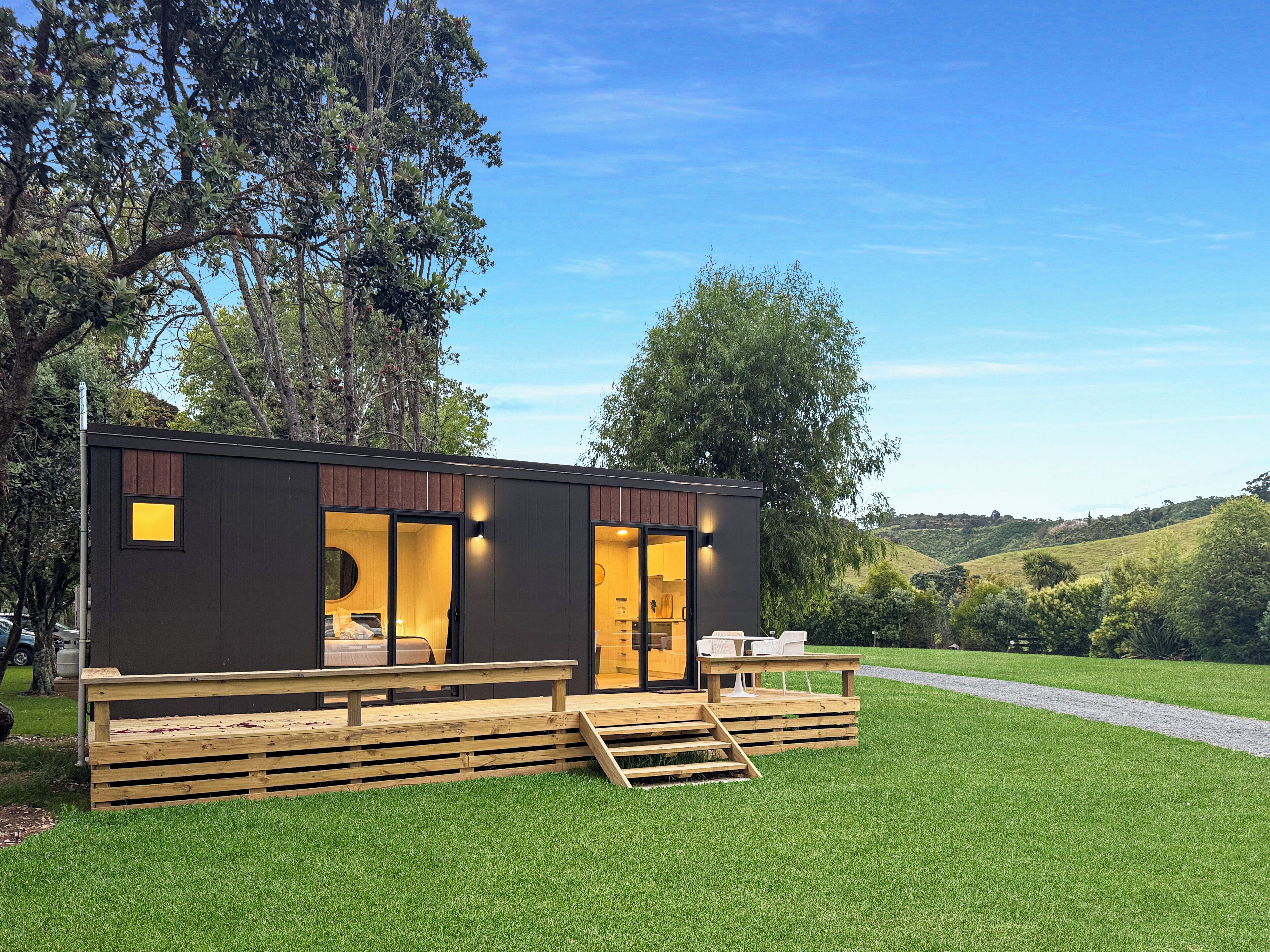 Une cabane moderne et compacte, dotée d’une terrasse en bois, de grandes fenêtres et offrant une vue sur le paysage environnant.