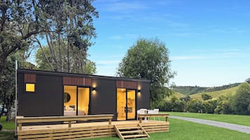Une cabane moderne et compacte, dotée d’une terrasse en bois, de grandes fenêtres et offrant une vue sur le paysage environnant.