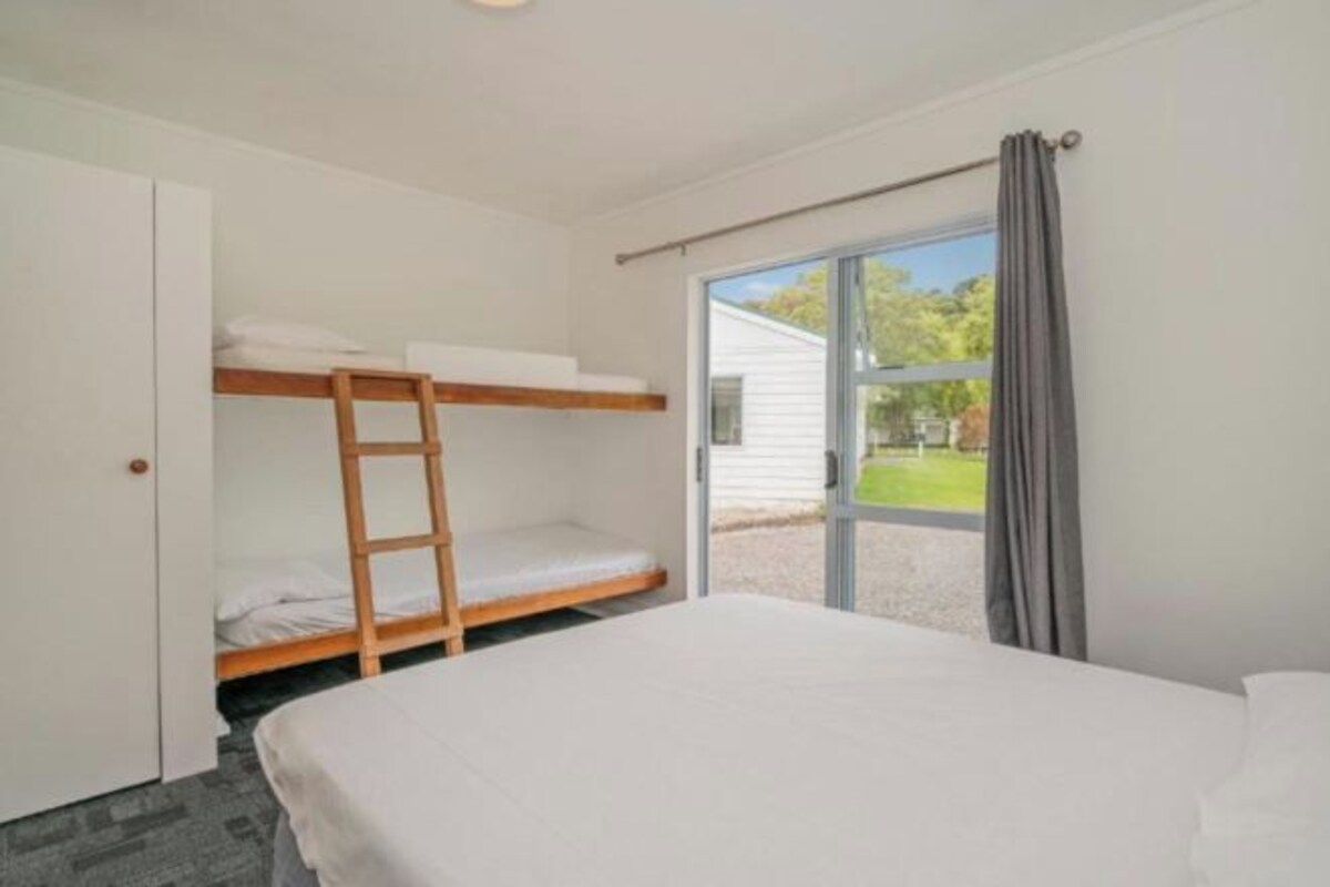 Un dormitorio con una cama litera, una cama individual, una ventana con vistas a zonas verdes y una puerta.