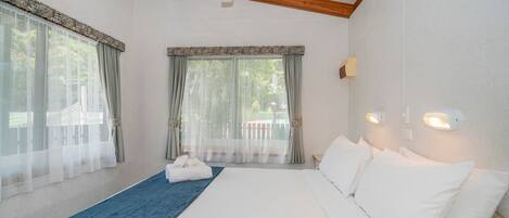 A bedroom with a large bed, a ceiling fan, and two windows with curtains.